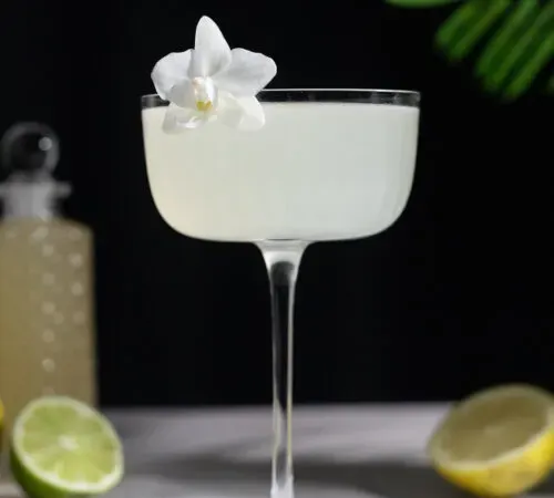 קוקטייל חיוור בכוס וינטג' ליד בקבוק סירופ זכוכית מפואר.' title=