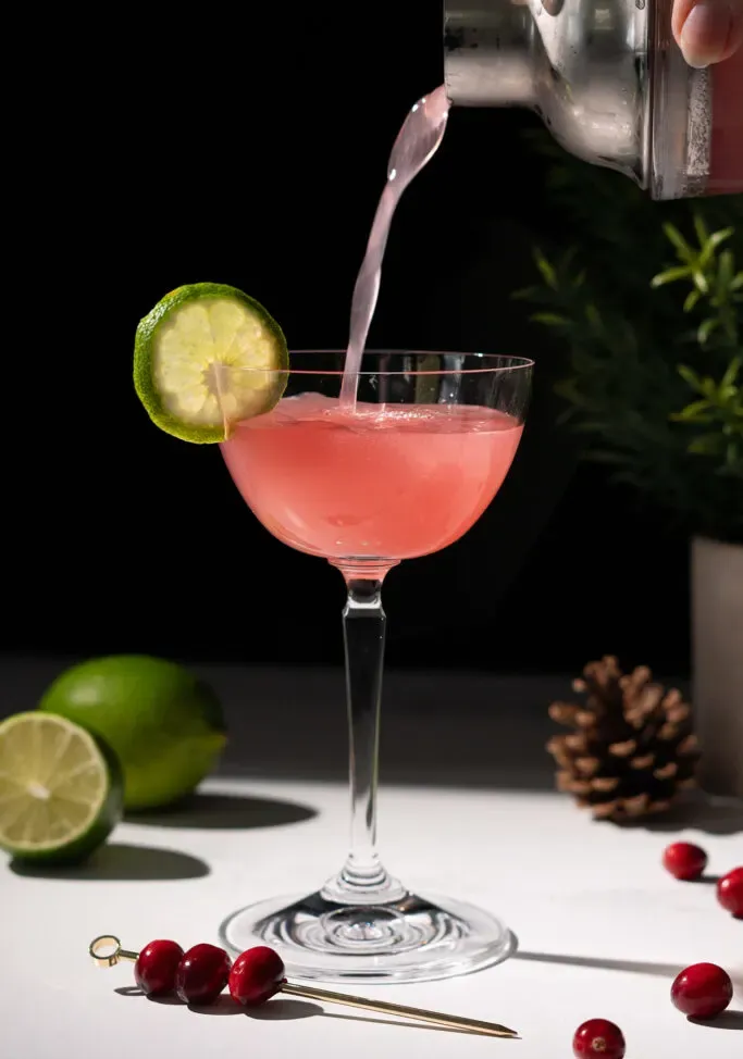 金属シェーカーからクーペ グラスに赤いカクテルを注ぎます。' loading='lazy' title=