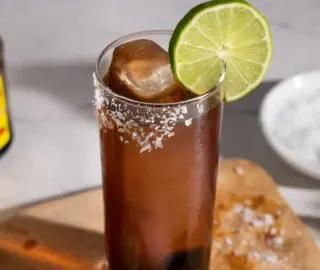 ein Longdrinkglas, gefüllt mit einem braunen Getränk.' title=