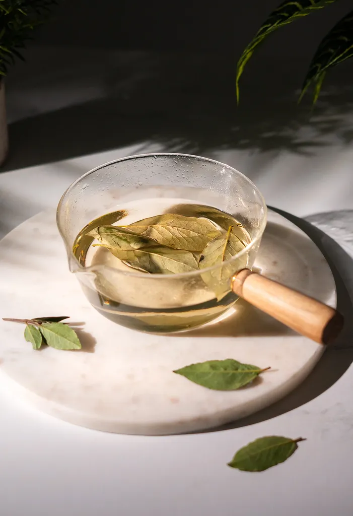 folhas de louro em calda em uma panela de vidro sobre um prato de mármore branco.' title=