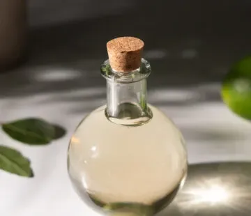 pequena garrafa redonda de vidro cheia de xarope verde claro ao lado de folhas de louro.' title=