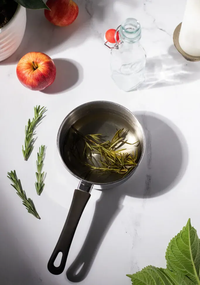 mały rondelek wypełniony klarownym płynem i kilkoma gałązkami rozmarynu.' title=