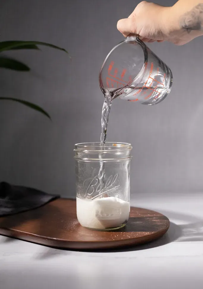 versando l'acqua da un misurino in un barattolo di vetro.' loading='lazy' title=