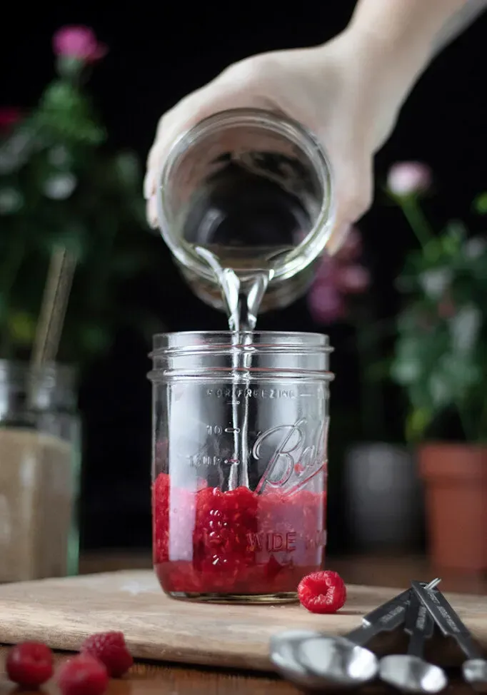 versando lo sciroppo semplice in un barattolo di vetro pieno di purè di frutti di bosco.' title=