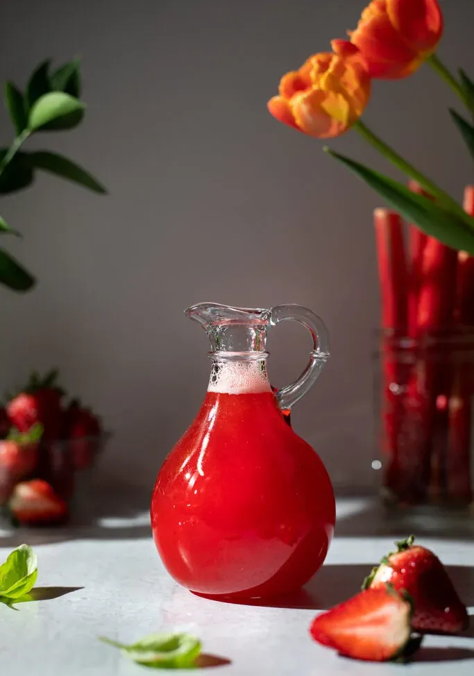 una piccola brocca di sciroppo di rabarbaro alla fragola rosso brillante.' title=