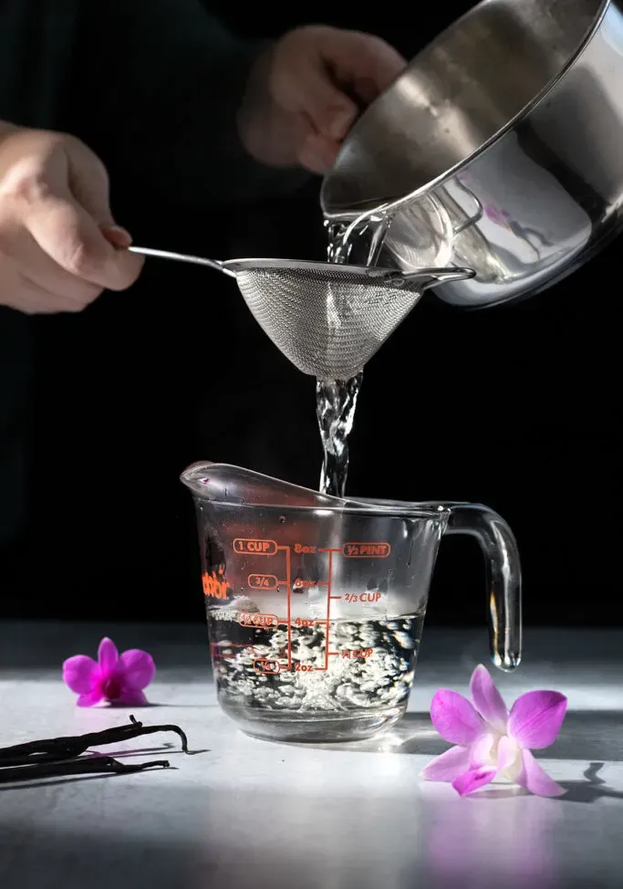 filtrando lo sciroppo di baccelli di vaniglia in un misurino.' title=