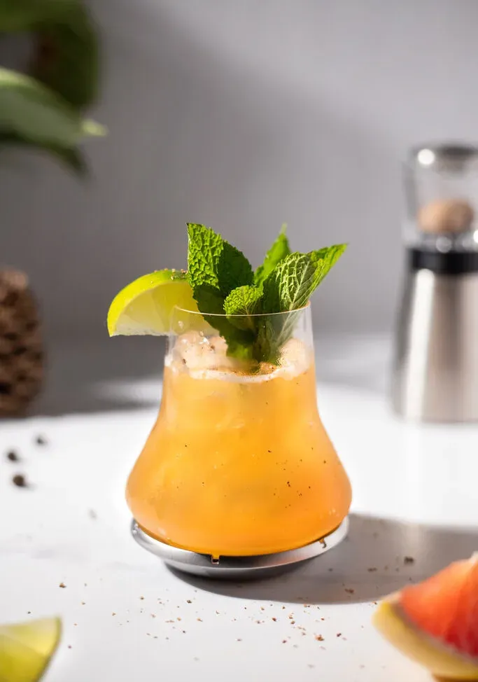 un cocktail de whisky et de pamplemousse garni d'un quartier de citron vert et de feuilles de menthe.' title=