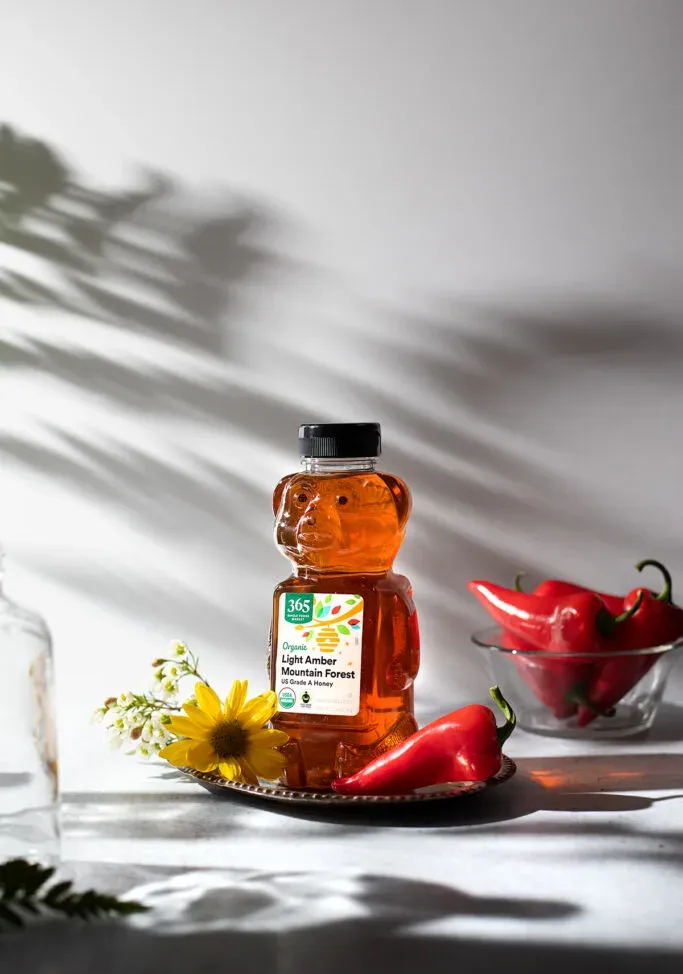 햇빛 아래 테이블 위에 있는 곰 모양의 꿀병' loading='lazy' title=