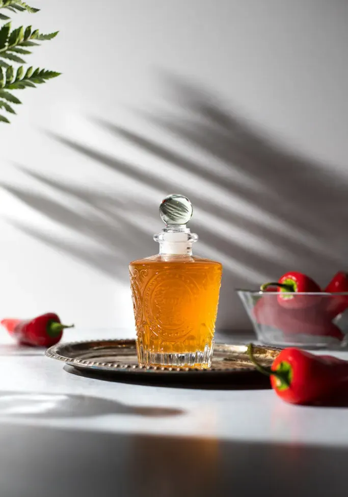 햇빛 아래 흰색 카운터에 황금빛 액체가 담긴 화려한 병' title=