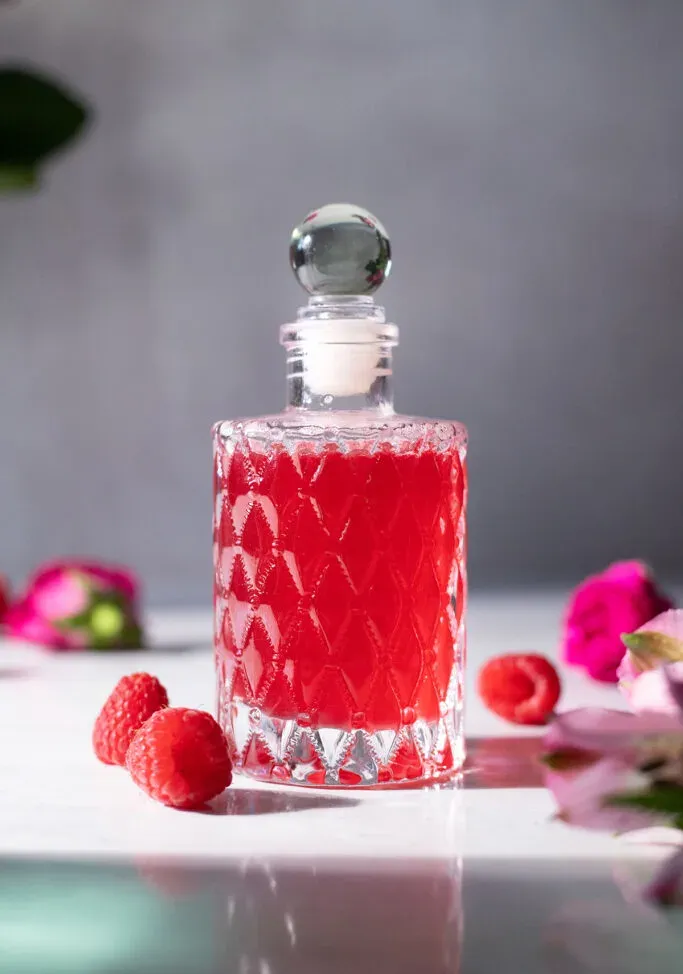 una elegante botella de vidrio llena de almíbar de color rojo brillante.' title=