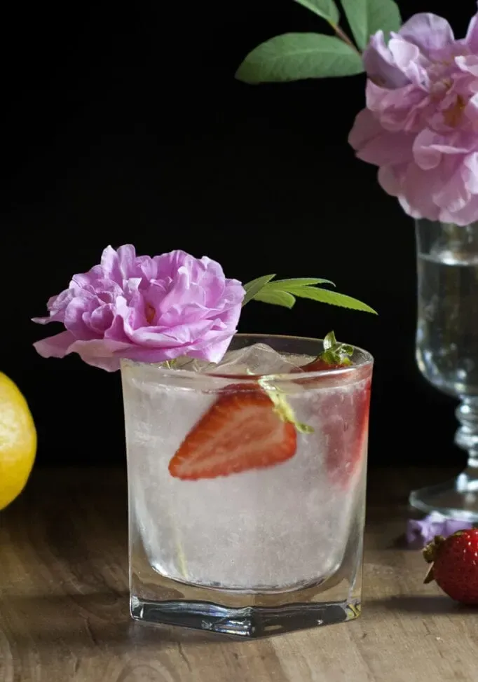 vaso bajo con limonada y rodajas de fresa adornado con una rosa rosa.' title=