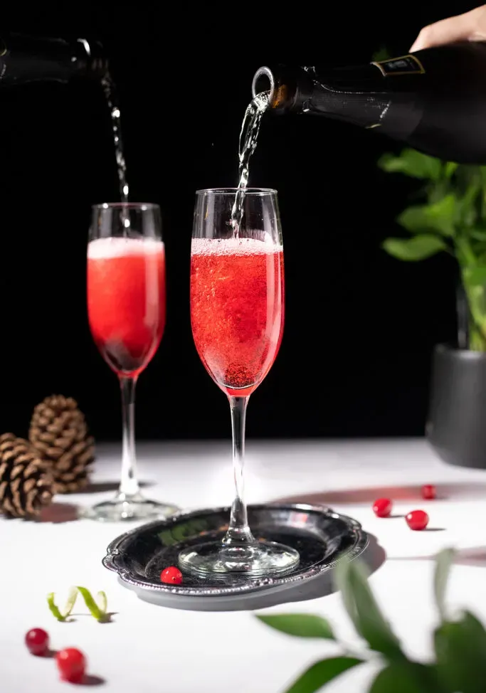 nalewanie wina musującego do soku z czerwonej żurawiny w kieliszkach do szampana.' title=