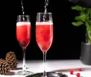 nalewanie wina musującego do soku z czerwonej żurawiny w kieliszkach do szampana.' title=