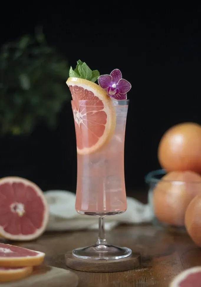 ein Hurricane-Glas, gefüllt mit einem rosa Cocktail und garniert mit einer Orchidee.' title=