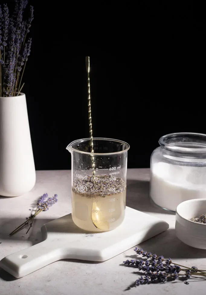 copo de vidro com botões de lavanda em calda e uma colher longa.' title=