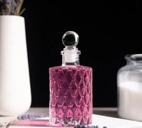 xarope roxo em frasco de vidro ao lado do buquê de lavanda.' title=