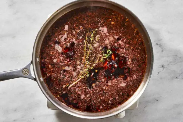 Uma frigideira com cenoura, aipo, cebola, alho, raminhos de tomilho e vinho tinto