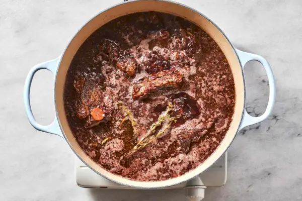 Um grande forno holandês com costelas douradas, marinada de vinho tinto e vegetais e caldo de galinha