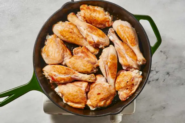 Une grande poêle avec des morceaux dorés de pilons et de cuisses de poulet sans peau
