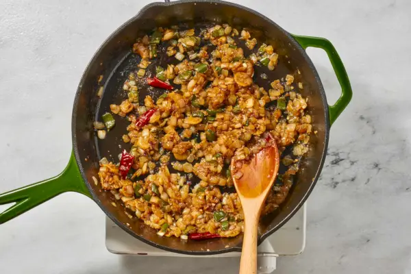 Une grande poêle avec des jalapeños, des piments rouges séchés, de l'oignon, de l'ail et du gingembre
