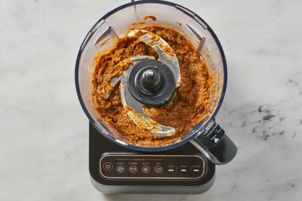 Un robot culinaire avec le mélange oignon-jalapeño réduit en purée avec du cumin, de la coriandre, des graines de fenugrec, de la cannelle, des clous de girofle, de la muscade, du paprika et du sel
