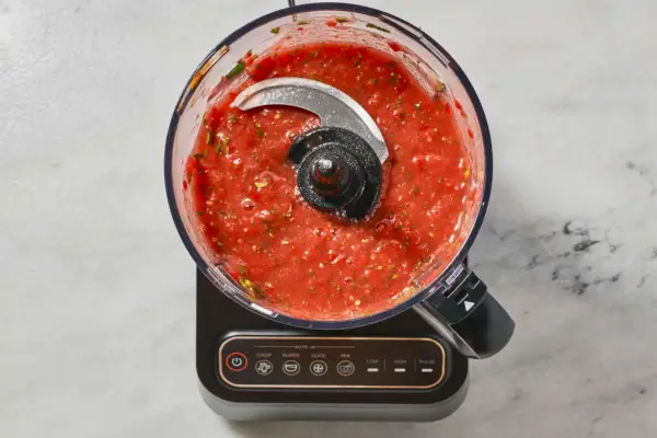Un robot culinaire avec des tomates hachées et de la coriandre, réduites en purée