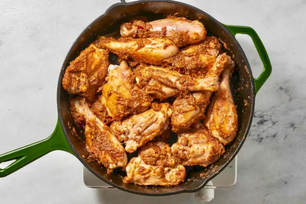 Une grande poêle avec des pilons et des cuisses de poulet dorés sans peau, cuits dans une sauce à l'oignon en purée