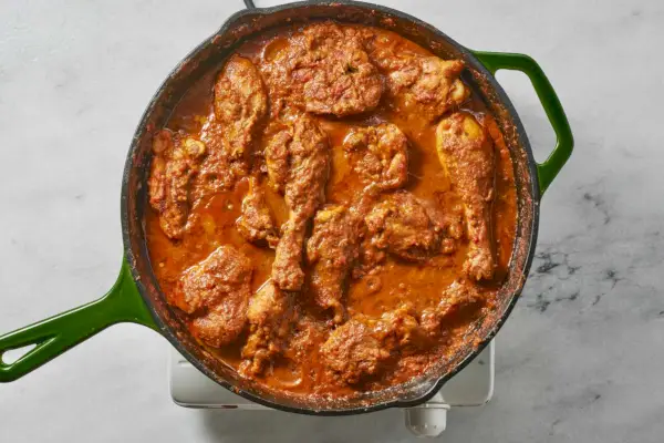 Une grande poêle de pilons et de cuisses de poulet cuits dans une sauce épicée au yaourt et aux tomates