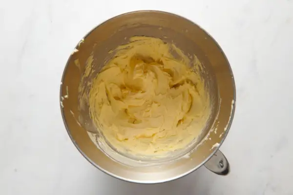 Un bol de batteur sur socle avec du beurre battu, du jaune d'œuf, de la vanille et du sucre en poudre