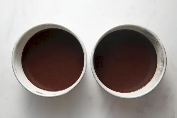 Deux moules à gâteau tapissés de papier sulfurisé et saupoudrés de farine avec une pâte à gâteau au chocolat