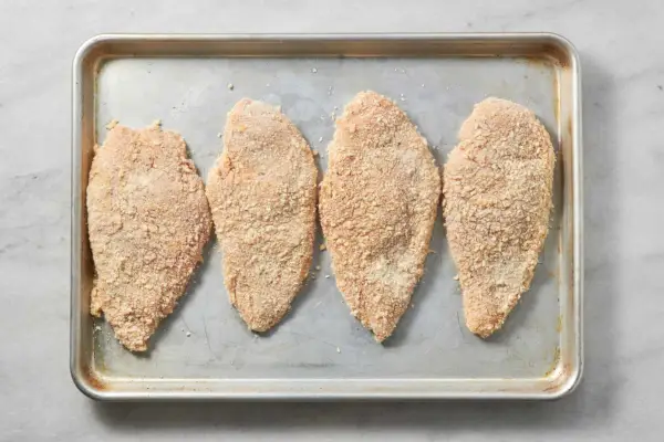 Ein Backblech mit vier panierten Hähnchenbrüsten