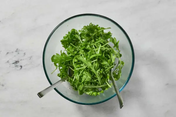 Eine kleine Schüssel Rucola, vermengt mit Olivenöl, Zitronensaft, Salz und Pfeffer