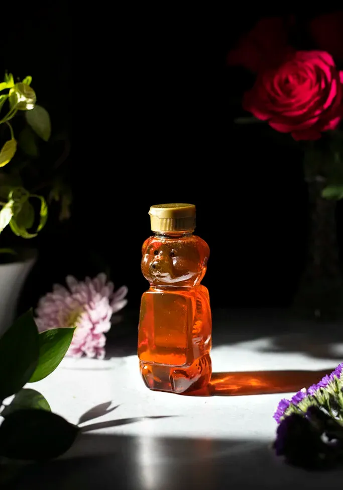 um recipiente de mel de urso de plástico próximo a flores.' loading='lazy' title=