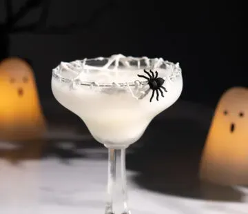 cocktail blanc avec garniture d'araignée à côté de bougies en forme de fantôme.' title=