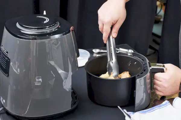 Personne utilisant des pinces pour ramasser du poulet dans une friteuse à air Ninja de 4 litres
