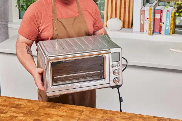 Une personne apportant la friteuse à air Breville the Smart Oven sur une surface en bois