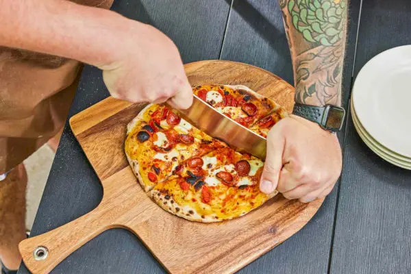Osoba krojąca pizzę maszyną Ooni Karu 12G