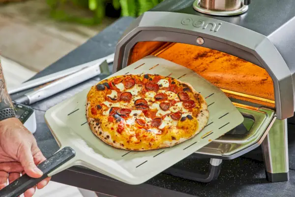 Ręka wyjmująca ciasto do pizzy z Ooni Karu 12G