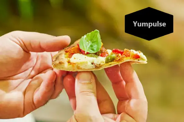 Dwie ręce trzymające kawałek pizzy przygotowanej w piekarniku Everdure KILN S Series