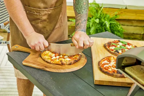 Osoba krojąca pizzę wykonaną w gazowym piecu do pizzy Ooni Koda 16