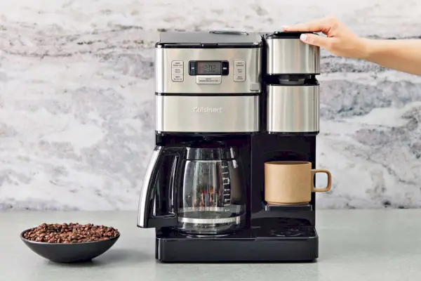 Laden Sie auf einer grauen Theke von Hand ein Kaffeepad in die Grind & Brew Plus-Kaffeemaschine des Cuisinart Coffee Center
