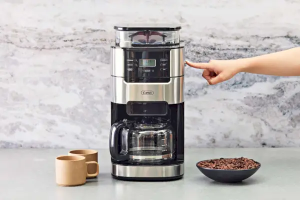 Drücken Sie mit der Hand einen Knopf an der Seite einer 10-Tassen-Filterkaffeemaschine von Gevi