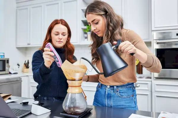Pessoa despejando água quente na cafeteira Chemex Classic Series enquanto outra pessoa mede a temperatura