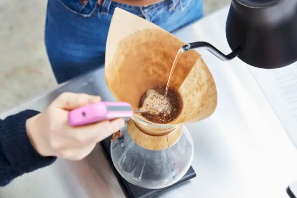 Pessoa despejando água quente na cafeteira Chemex Classic Series enquanto outra pessoa mede a temperatura