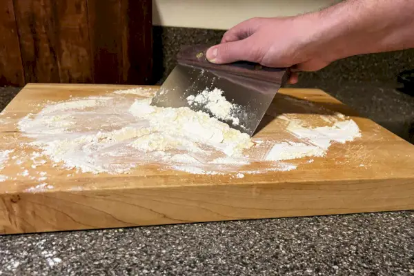 Une personne étalant de la farine à l'aide du couteau d'établi de la King Arthur Baking Company