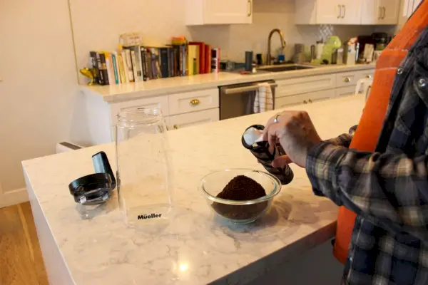 Uma pessoa coloca café moído no filtro da cafeteira Mueller Cold Brew