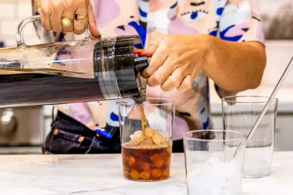 Uma pessoa derrama café frio feito na cafeteira Mueller Cold Brew em um copo de gelo