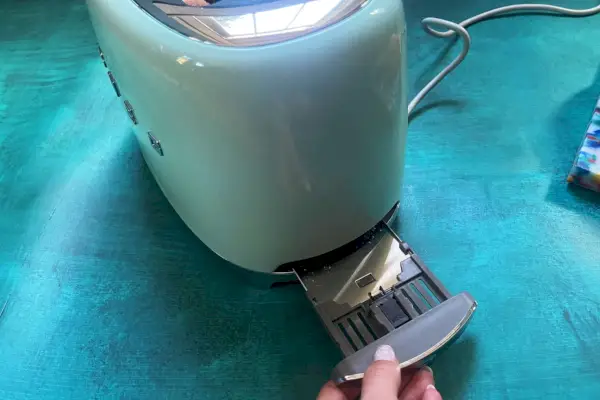 SMEG 2슬라이스 토스터(TSF01PGUS) 아래 슬롯에 부스러기가 있는지 확인하는 사람
