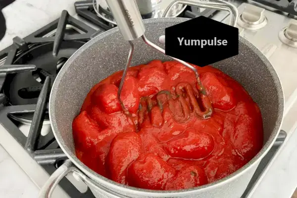 Um indivíduo usa o espremedor de alimentos de aço inoxidável de silicone Tovolo para amassar tomates em uma panela.