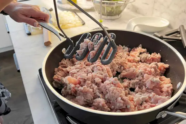 Um indivíduo usa o espremedor de alimentos de aço inoxidável de silicone Tovolo para amassar uma refeição no fogão.